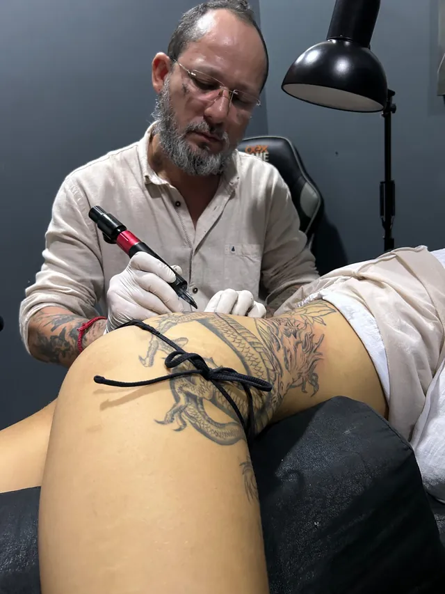 Tatuador da Pimenta Tattoo tatuando a coxa de um cliente com máquina rotativa