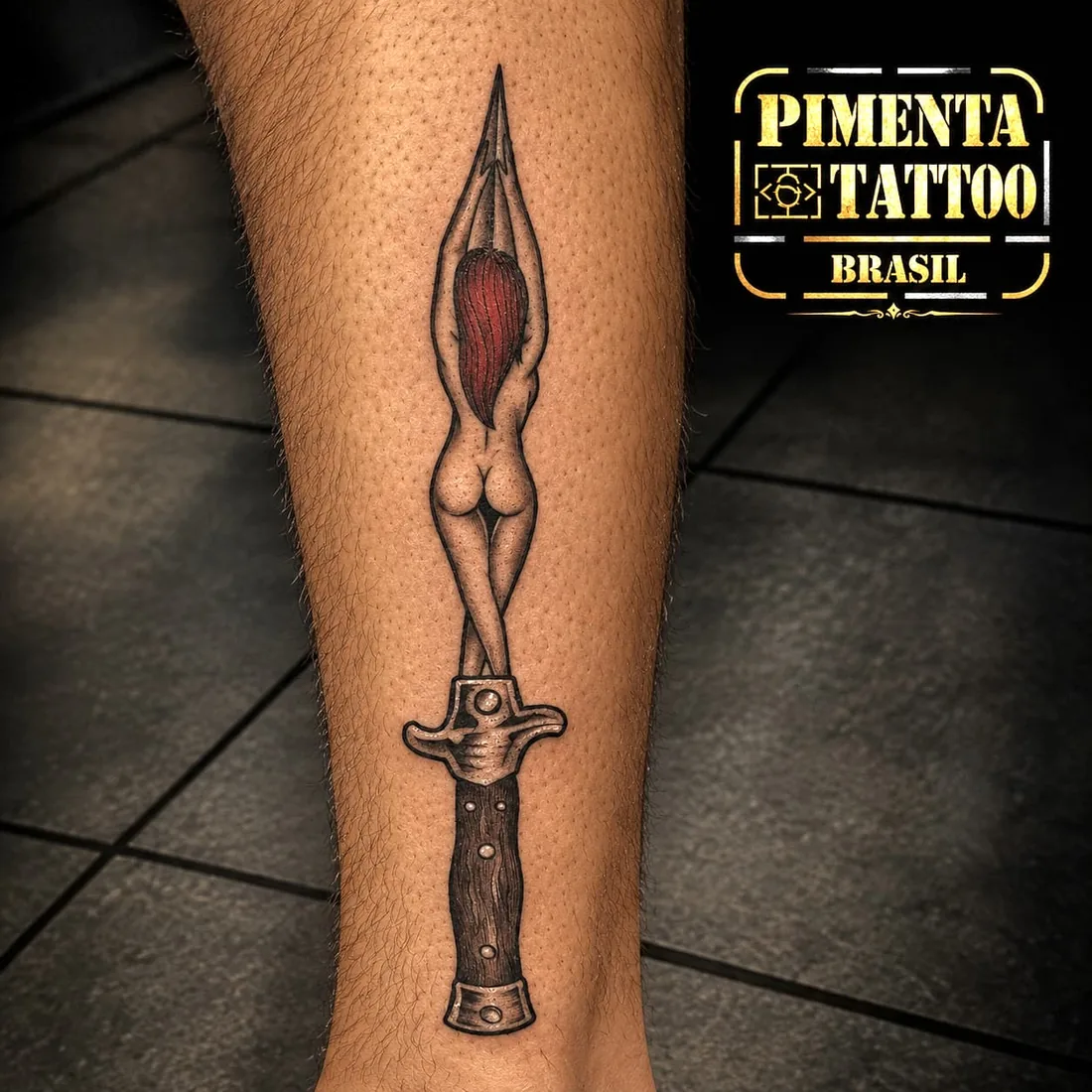 Tatuagem de adaga com figura feminina estilizada, na perna