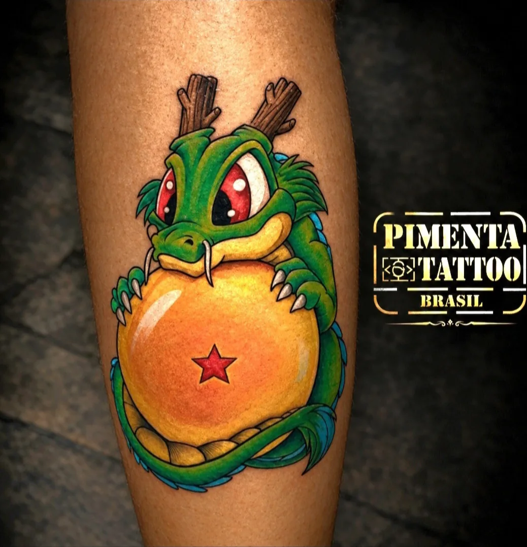 Tatuagem colorida de dragãozinho cartoon abraçando uma esfera de uma estrela, na perna