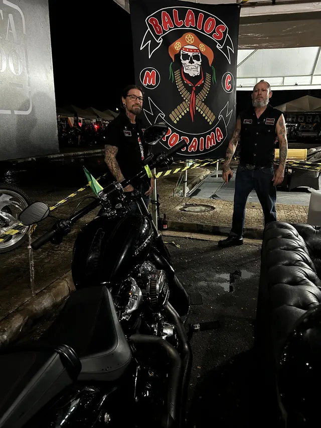 Encontro noturno de motociclistas, com motocicletas estacionadas em frente a um estandarte