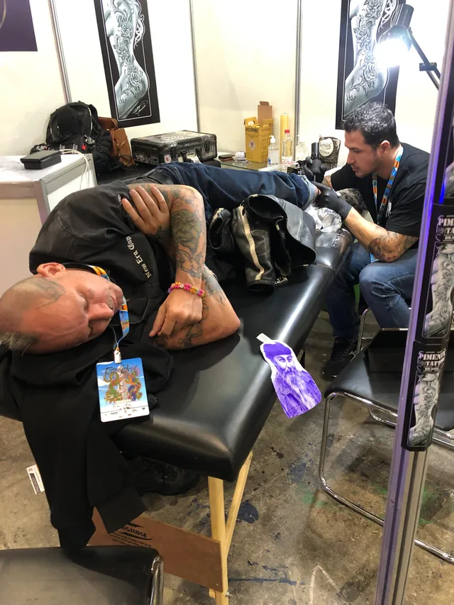 Sessão de tatuagem durante evento, com o cliente deitado na maca